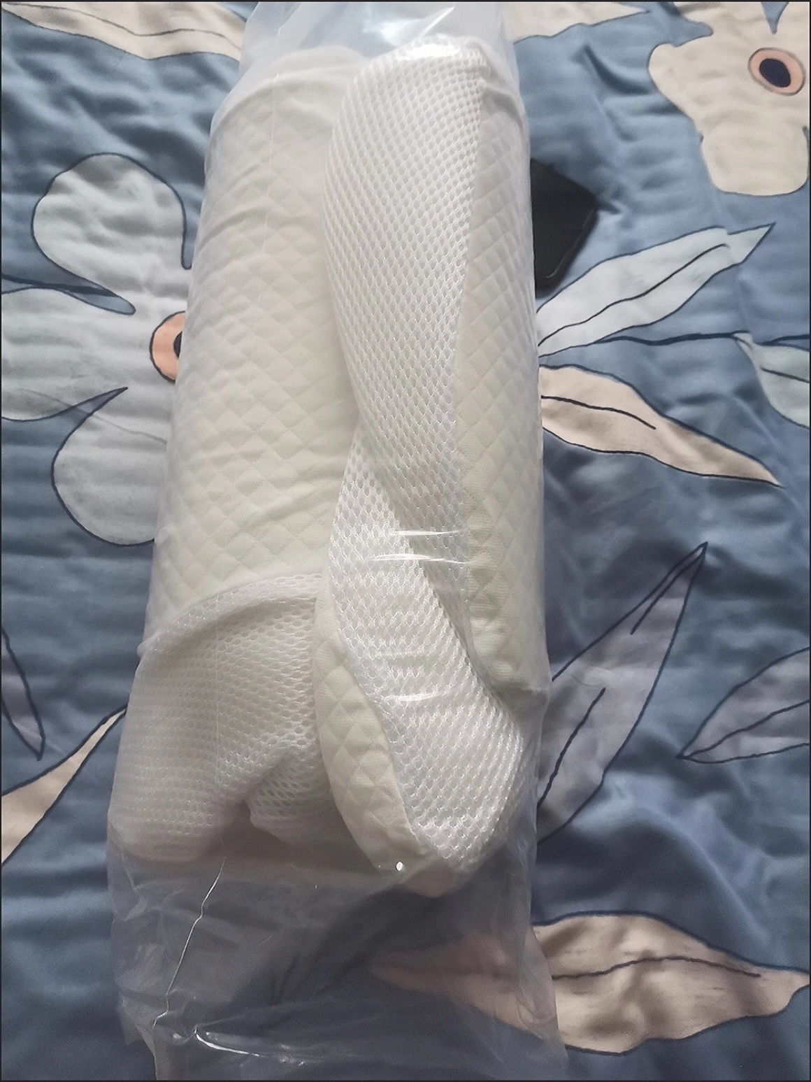 White textured pillow in clear plastic packaging on a floral bedspread